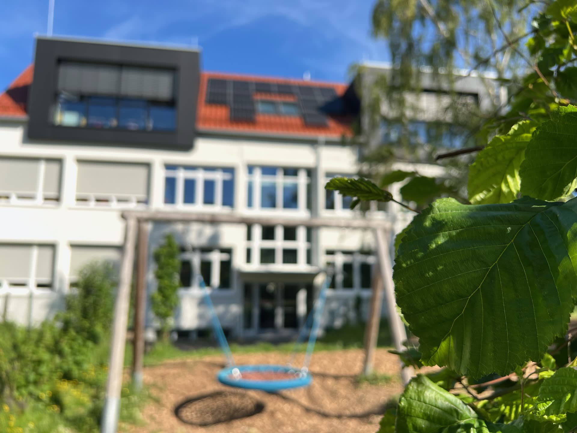 Schulhaus der Grundschule am Jakobsberg mit Schaukel, blauem Himmel und Gr&uuml;nanlage